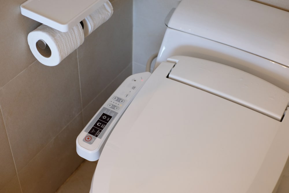Buttons of a electronic white toilet washlet with warm light and blurred restroom brown floor background,automatic modern flushing toilets