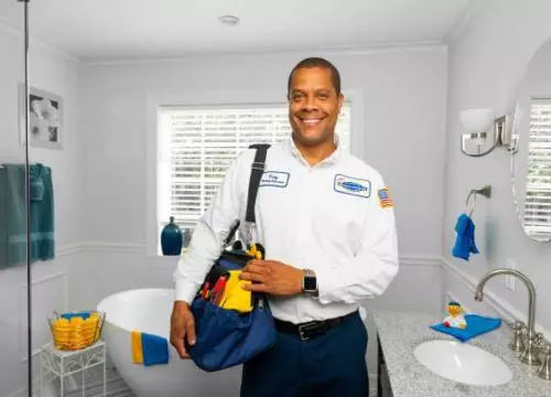 Technician smiling standing in bathroom with tool bag on shoulder