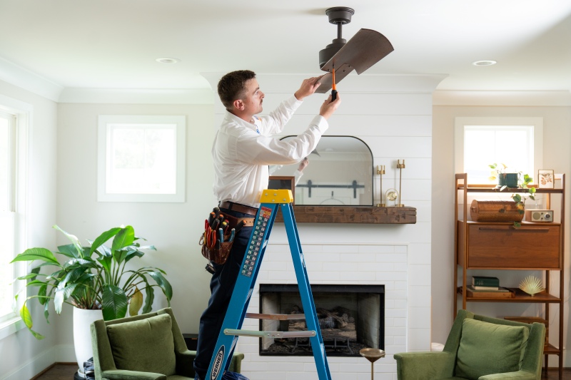 Technician on ladder installing ceiling fan 