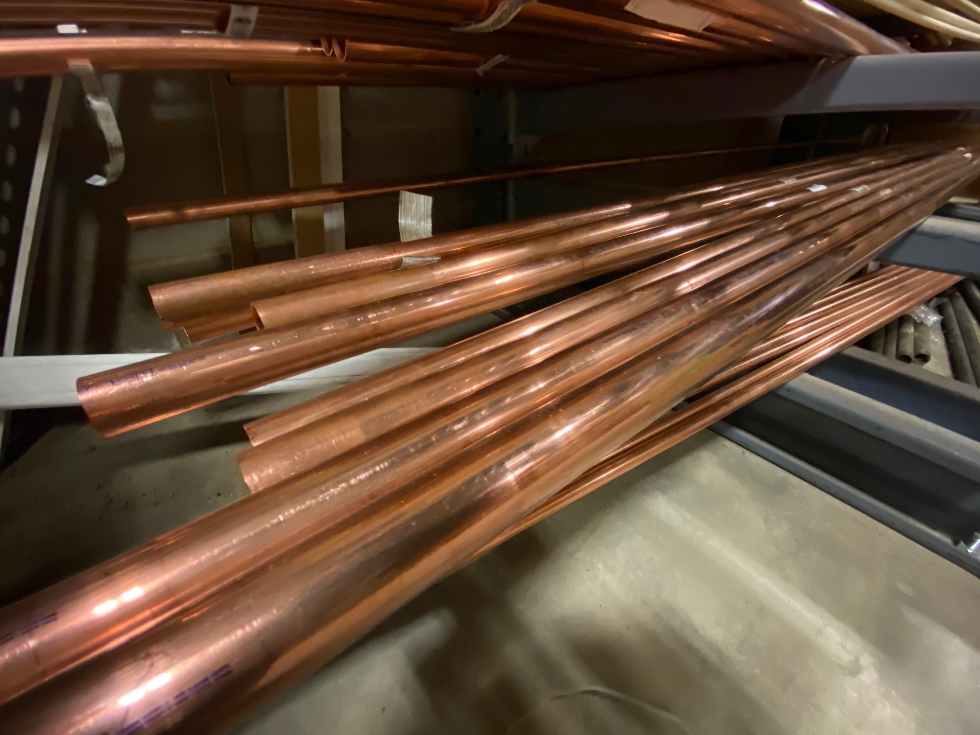 Several copper pipes stacked horizontally on metal shelving in a storage area.