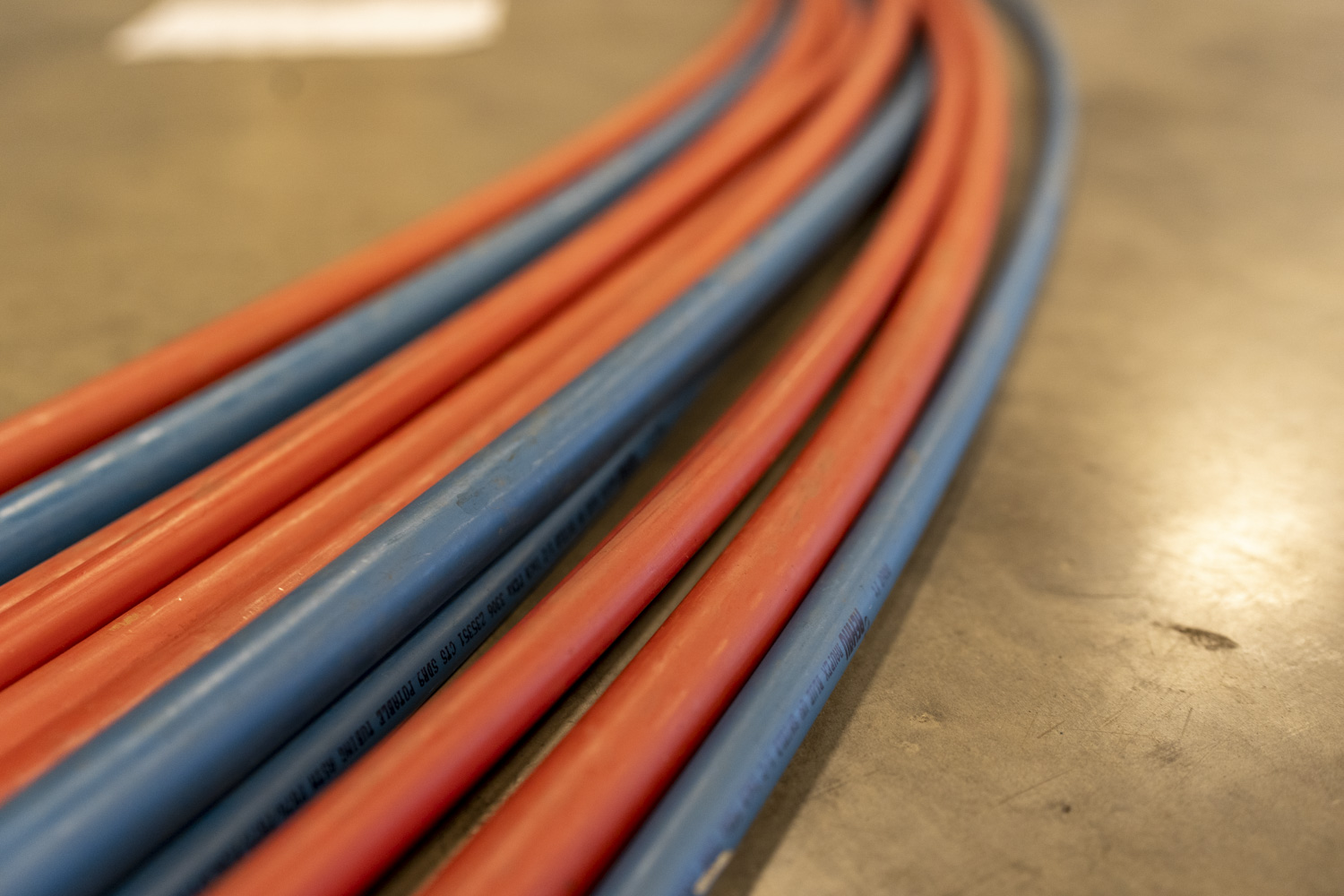 Close-up of blue and red plastic pipes or tubing lying parallel on a smooth, light-colored floor surface.