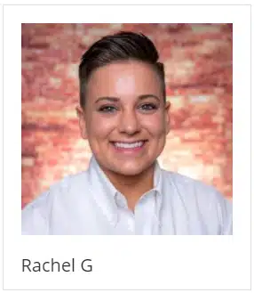 Rachel g is smiling in front of a brick wall.