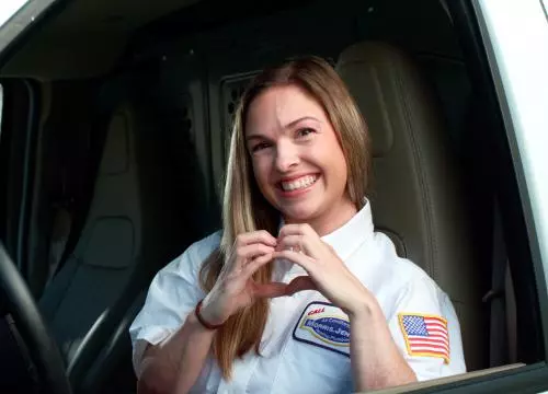 A woman is driving a truck and making a heart gesture.