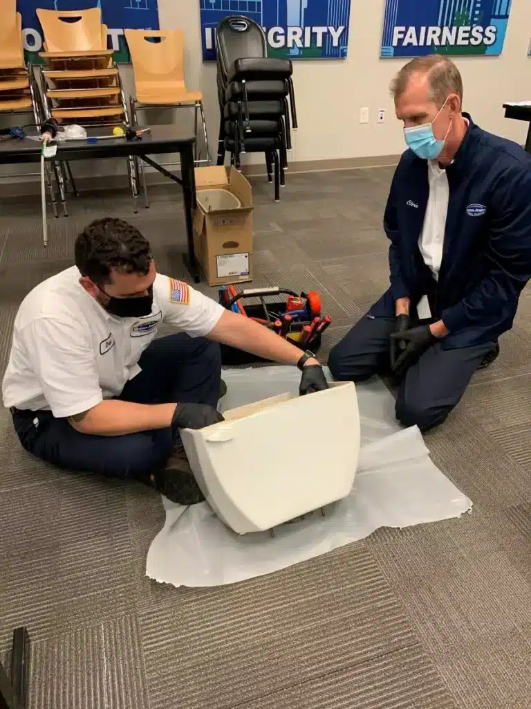 Plumber trainee and teacher working on a toilet tank.