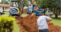 A man digging a hole in a yard with an excavator.
