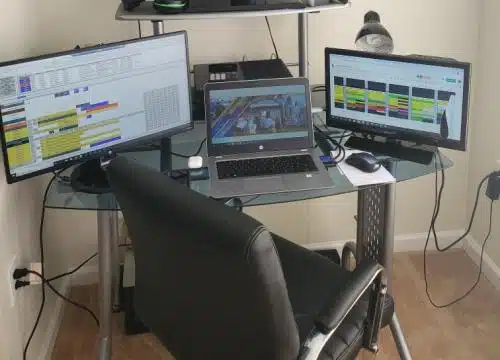 A computer desk with three monitors and a chair.