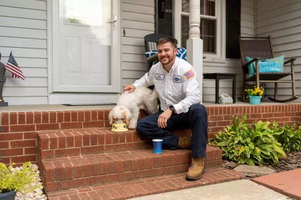 A man sitting on the steps of a house with a dog.