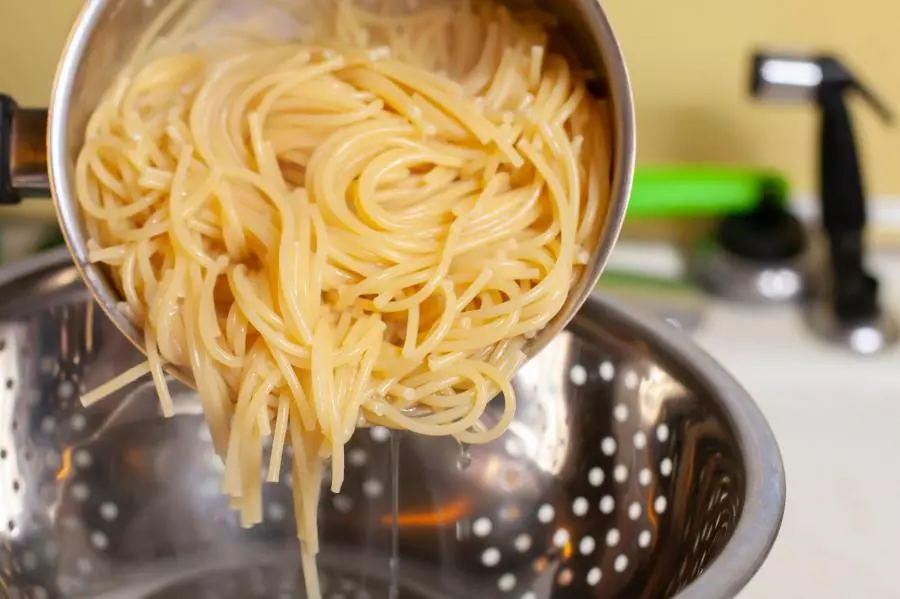 Pasta being drained in a metal colander.