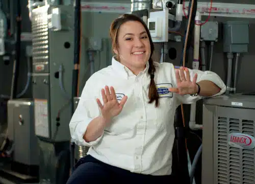 morris jenkins female tech next to some ac and heating units. holding her hands up in a "wait" position.