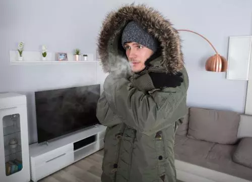A man in a parka is standing in front of a tv.