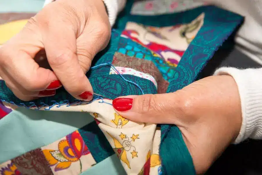 A woman is sewing a quilt on a table.