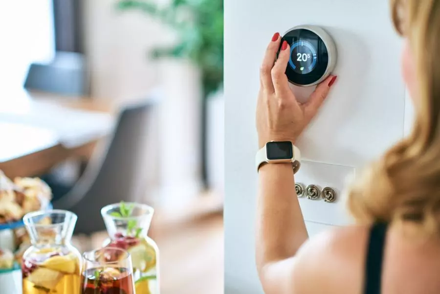A woman is using a smart thermostat in a kitchen.