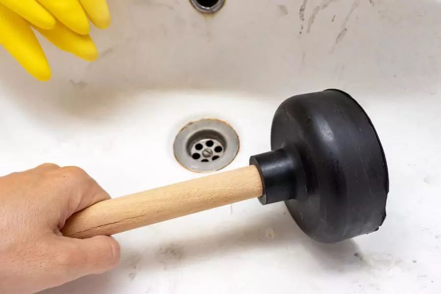 A man using a plunger to clean out the drain clog.