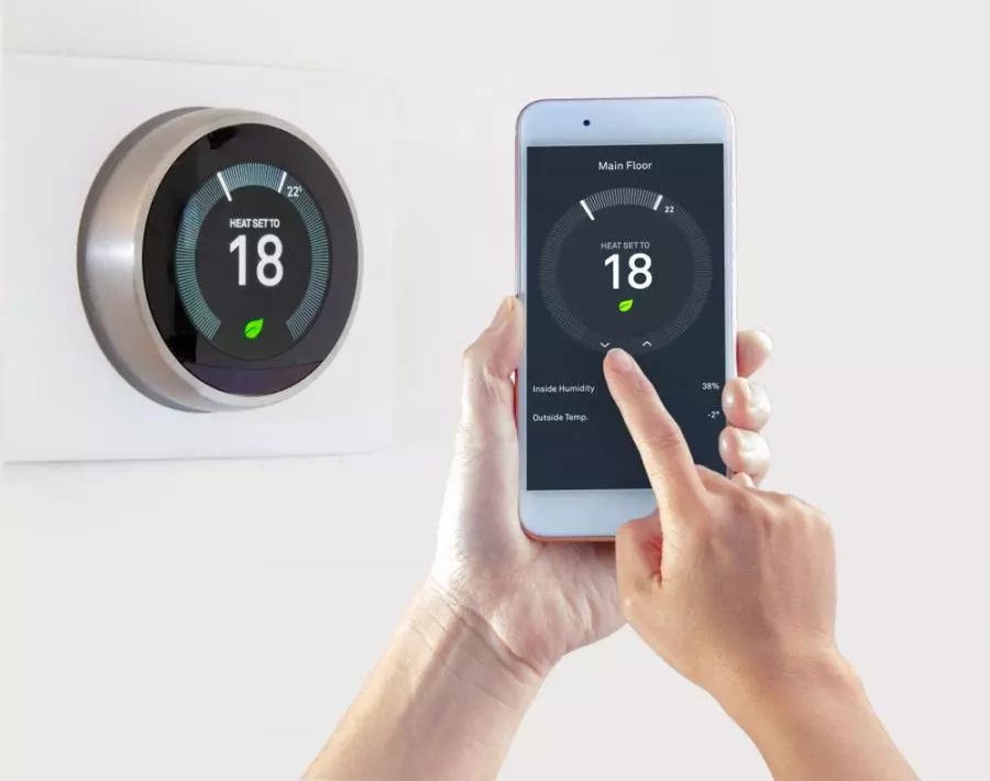 A person using a smartphone to control a nest smart thermostat