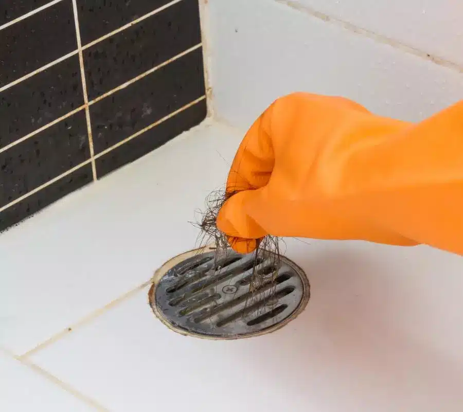 A person in orange gloves cleaning a drain in a bathroom.