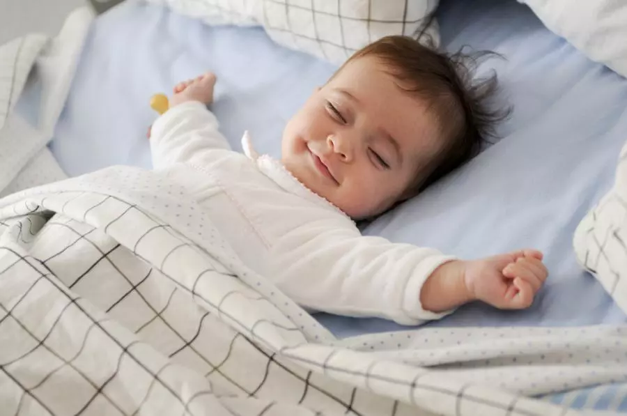 A baby is sleeping in a bed with a blanket.