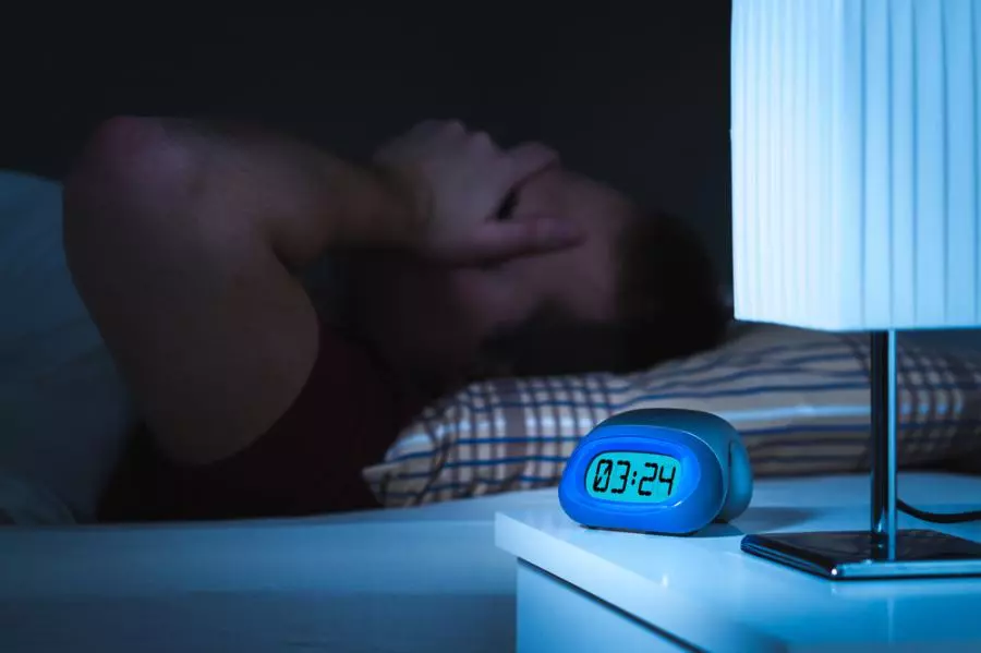A man laying in bed with a blue alarm clock.
