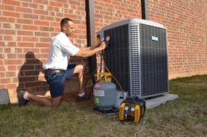 A man working on an air conditioner in front of a brick wall.