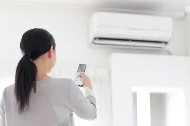 A woman holding a remote control in front of an air conditioner.