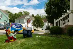 A woman kneeling down in front of a lawn mower.