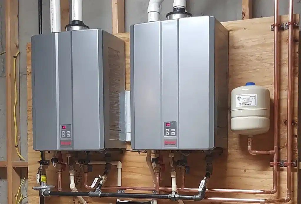 Two water heaters in a room with pipes.