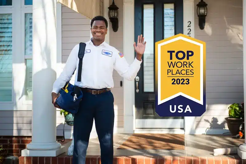 A man is standing in front of a house with a top work place award.
