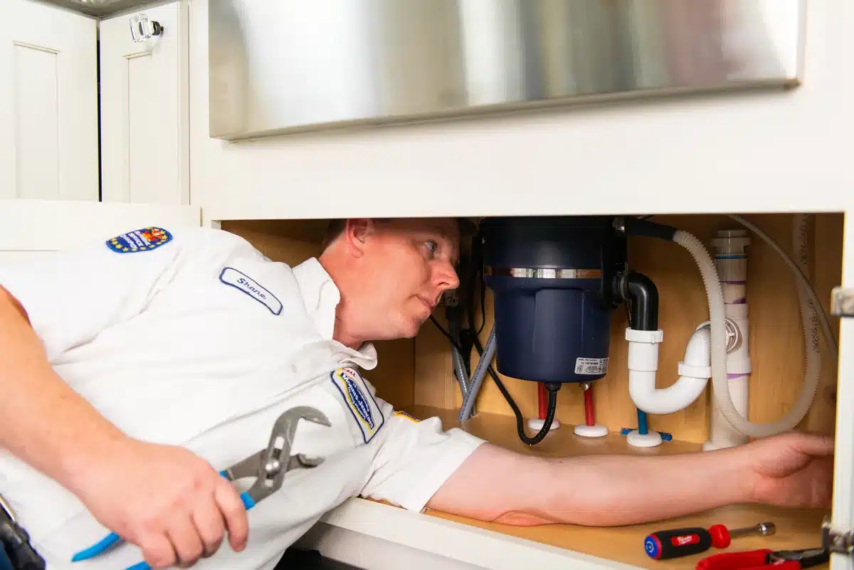 A plumber repairing a sink under a cabinet.