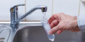 A hand is holding a water tap in a kitchen sink.
