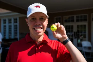 A man in a red shirt holding a golf ball.