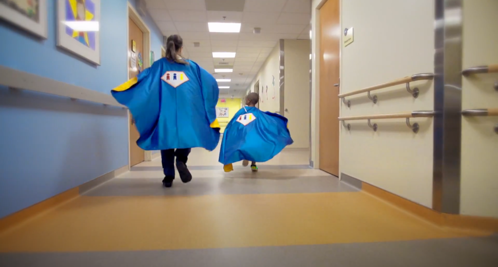 Two children dressed as superheroes walking down a hallway.