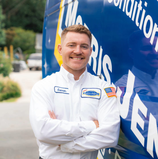 Person in a white uniform stands with arms crossed, smiling in front of a blue service van with partial text visible.