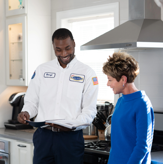 A man in a uniform shows a document to a woman in a kitchen. Both are smiling and appear to be discussing something.