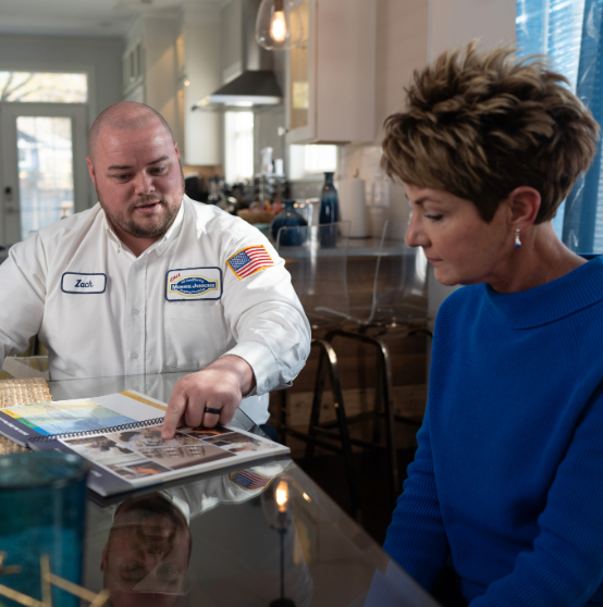 Person wearing a company uniform shows a woman a brochure at a kitchen table.