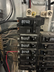 Close-up view of an electrical breaker panel with several circuit breakers, wires, and bus bars visible. Two heavy-gauge black wires are connected at the top.