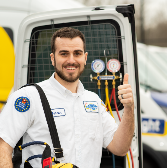 A male HVAC technician in uniform stands by a service van, holding tools and giving a thumbs-up gesture, with pressure gauges visible in the background.
