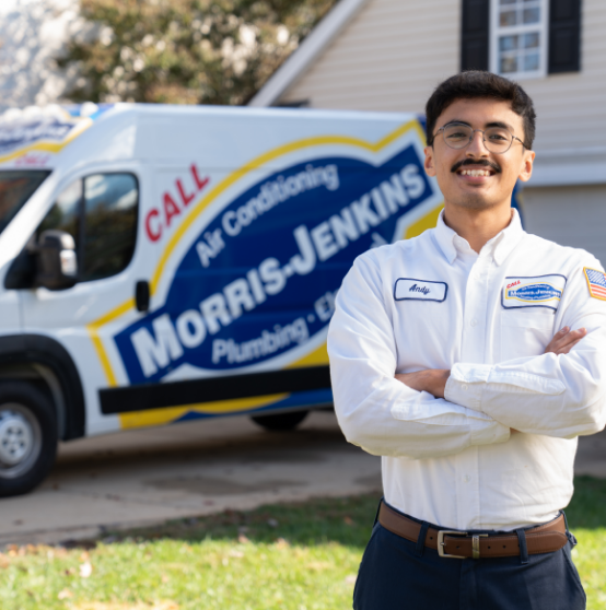 A man in a Morris-Jenkins uniform stands with arms crossed in front of a Morris-Jenkins service van parked in a residential driveway.