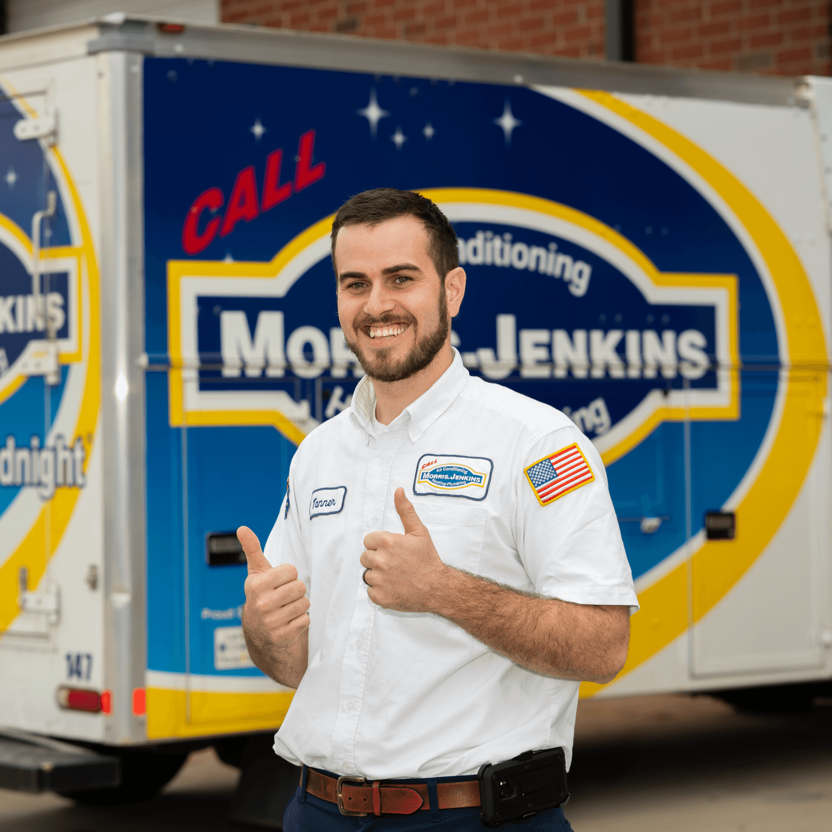 A man in a uniform stands outside, smiling and giving two thumbs up in front of a branded Moore-Jenkins service van.
