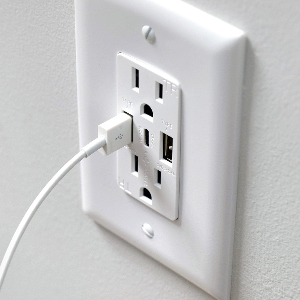 A white wall outlet with two standard power sockets and two USB ports, with a USB cable plugged into one of the USB ports.