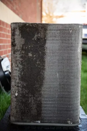 A dirty air conditioner in front of a brick wall.